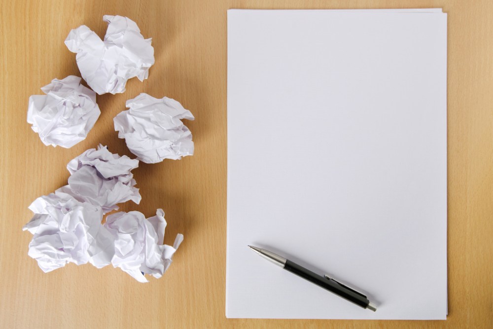 Evidence of going nowhere with writing. An empty sheet of paper and a pile of crumpled up ones.