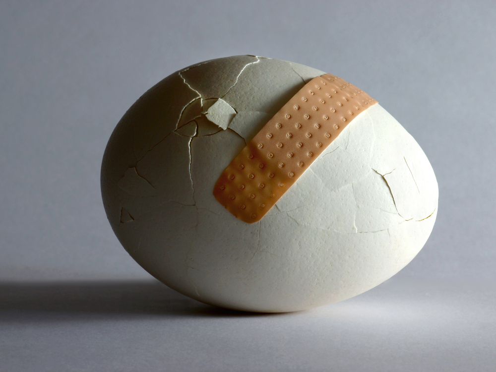 an egg with a bunch of cracks and an ineffective bandaid across a few of them.