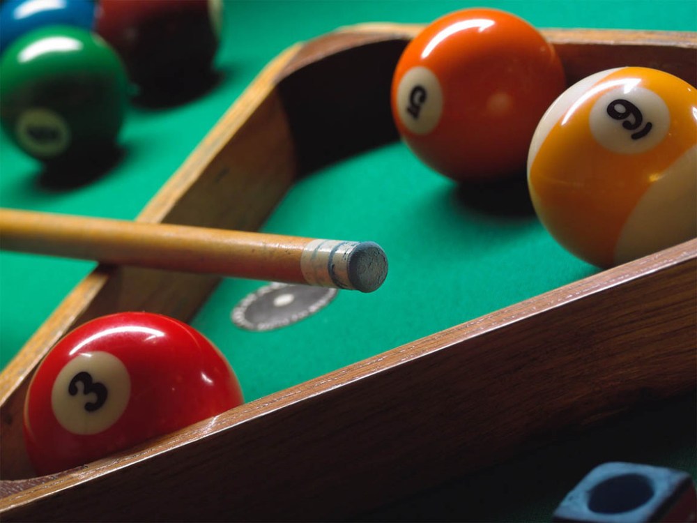 A triangle, a pool cue and a few balls inside the triangle and a few balls outside the triangle. The table is green. The balls in the triange are 3, 5 and 9. Nine is striped.